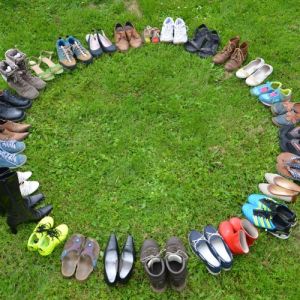 viele Schuhe im kreis aufgestellt und von oben fotografiert. Untergrund ist eine grüne Wiese.